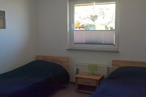 A room with two single beds, a small bedside table with a lamp, and a window with blinds. - Holiday home in Osburg with swimming pool (Osburg)