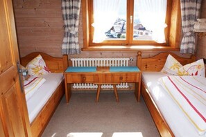 Ein kleiner Holzraum mit zwei Betten, einem Fenster mit Vorhängen und einer Heizung.