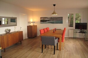 Ein moderner Essbereich mit einem Holztisch, roten Stühlen, einem grauen Stuhl, einem Schrank, einem Fernseher und einem Bild an der Wand.