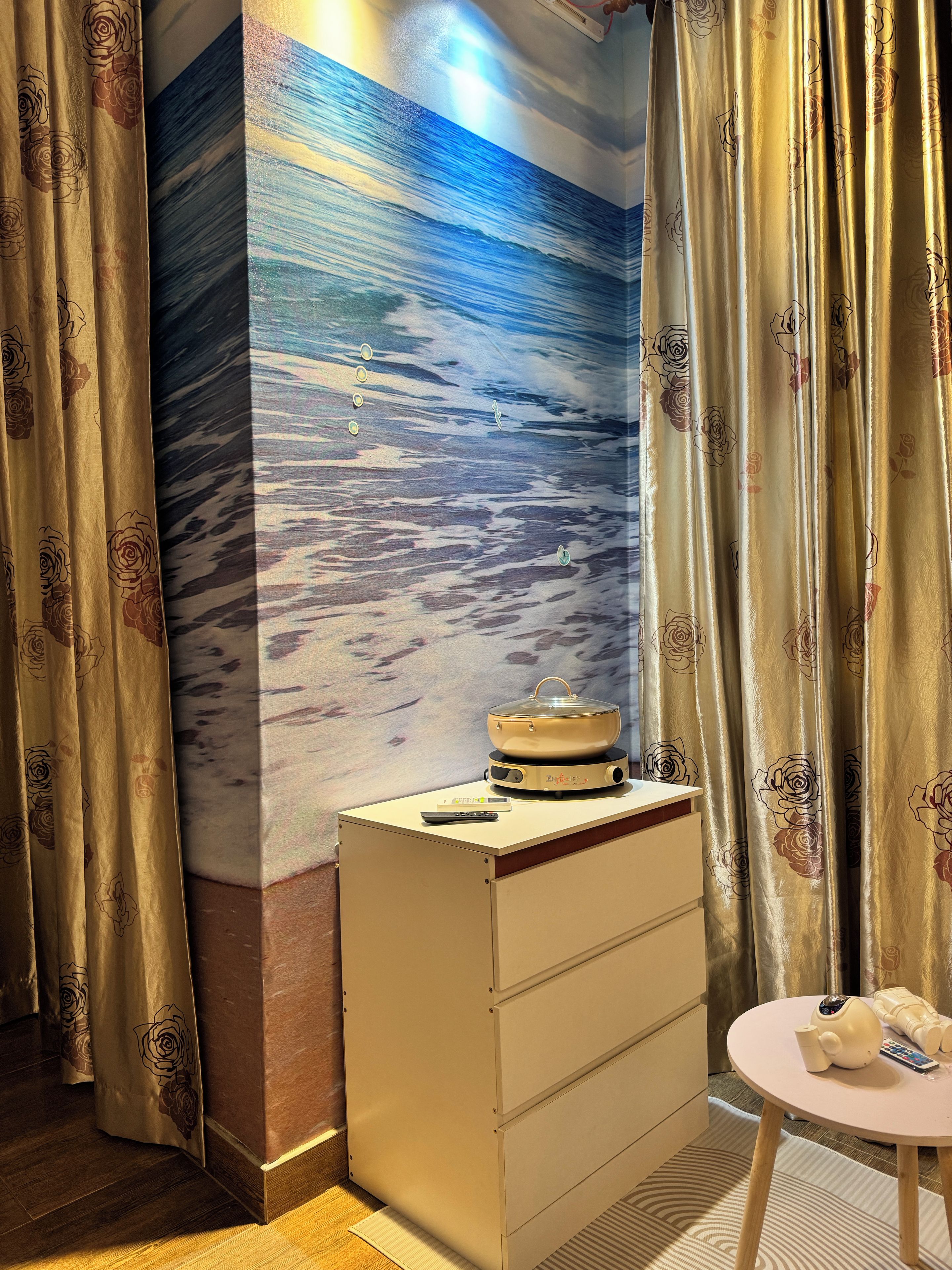 Ein Zimmer mit Wandgemälde, einem kleinen Tisch mit Teekanne und einem Schrank.