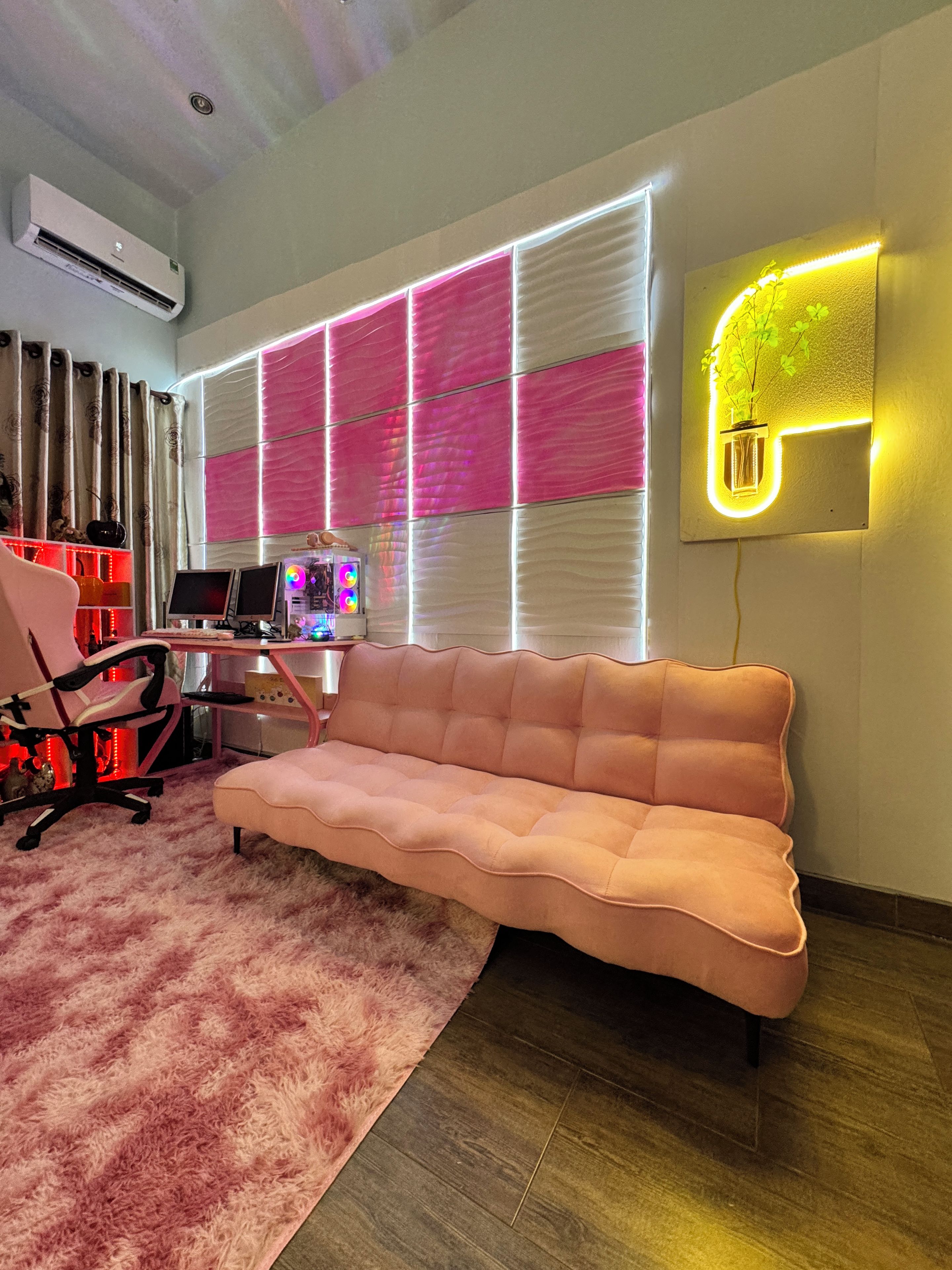 Una sala de estar moderna con un sofá rosa, un escritorio con una computadora y un aplique de pared.