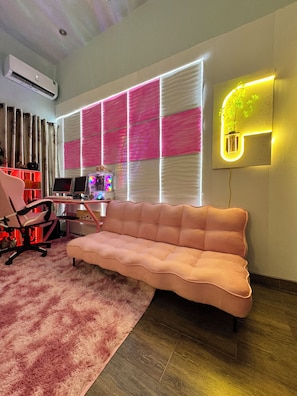 Una sala de estar moderna con un sofá rosa, un escritorio con una computadora y un aplique de pared.