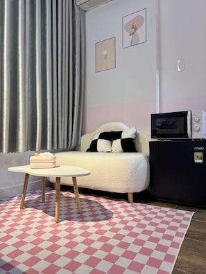 A room with a sofa, a small table, a microwave, and a refrigerator.
