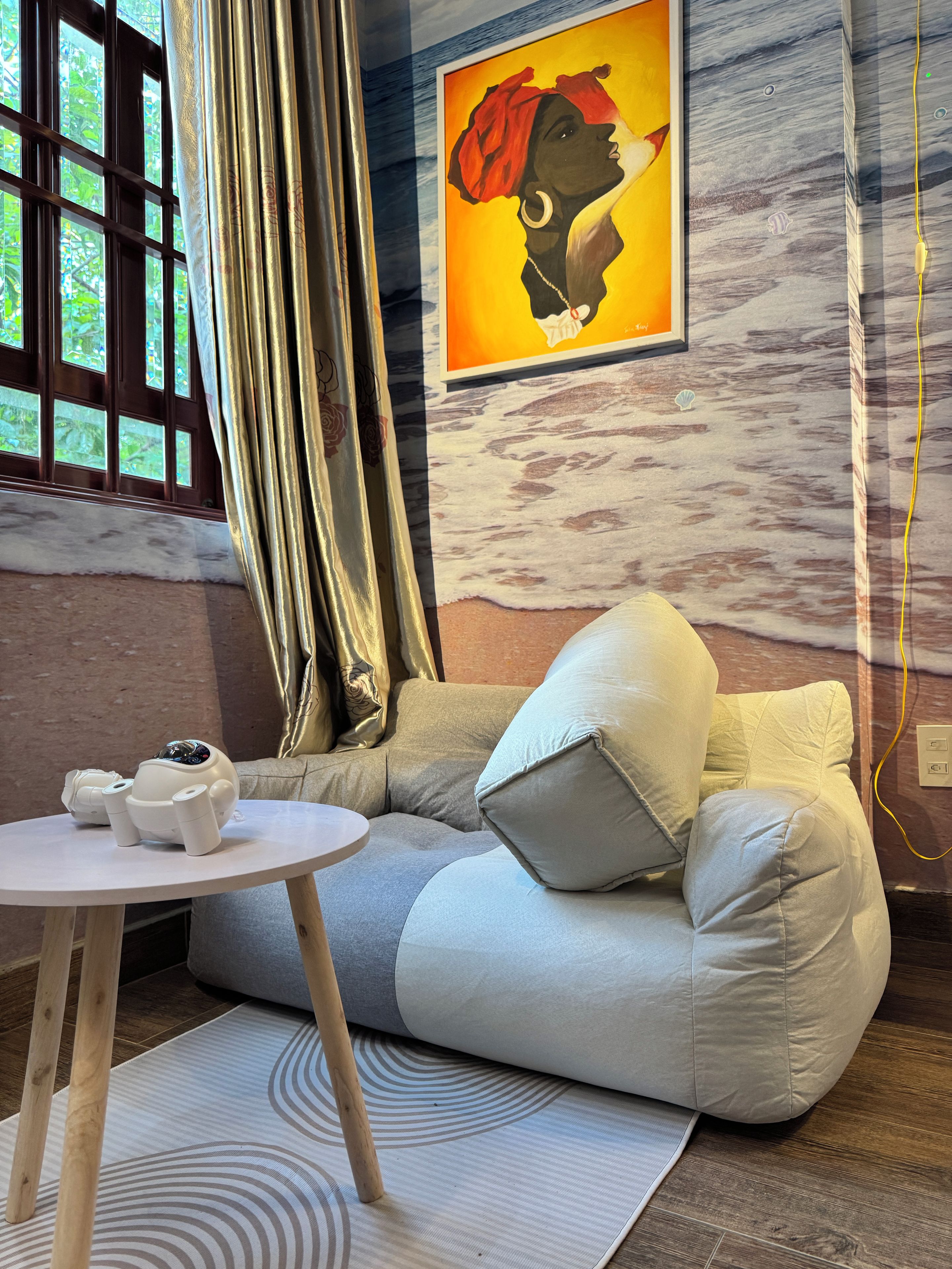 Ein Zimmer mit einer Couch, einem kleinen runden Tisch, einem Gemälde und einem Fenster mit Vorhängen.