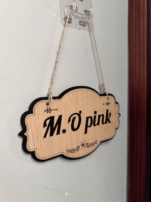 Un letrero de madera con el nombre 'M. O pink' colgado en una pared.