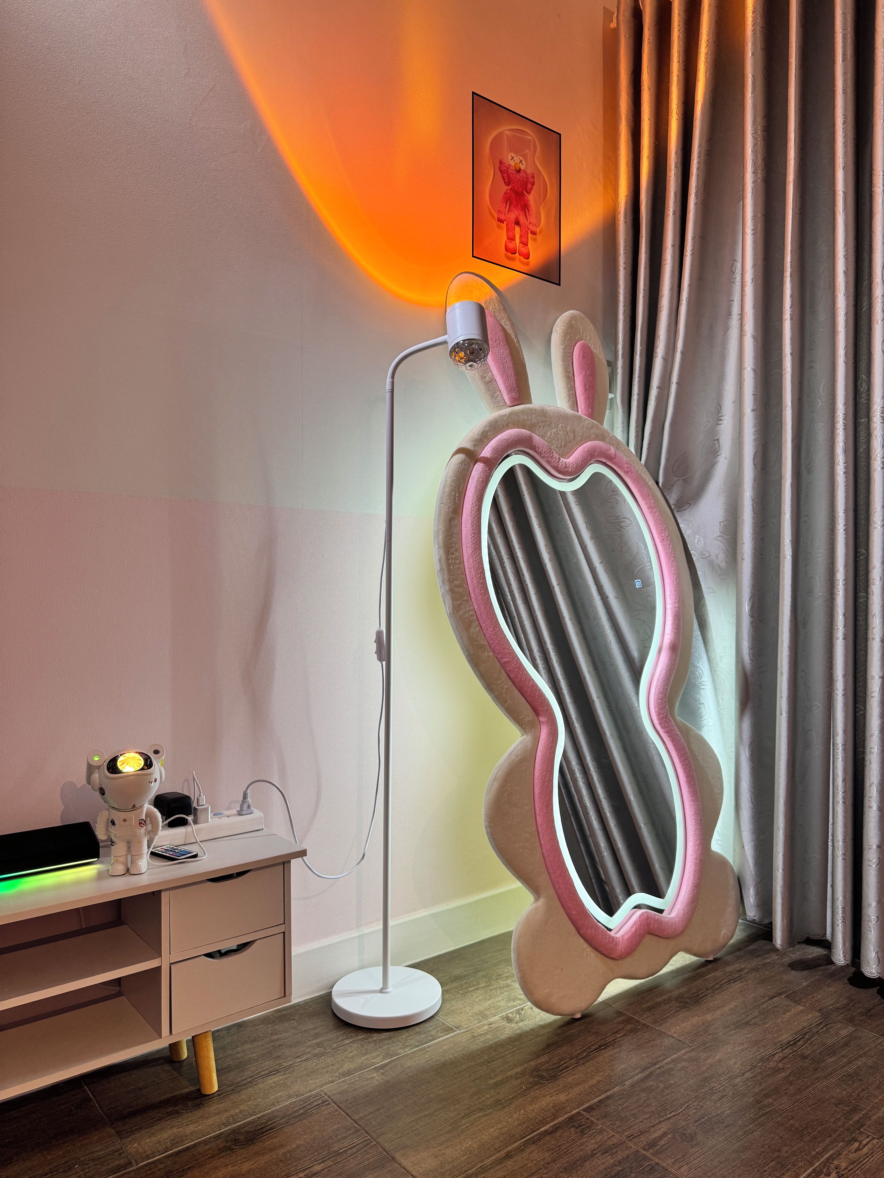 A room with a desk, a standing lamp, a plush toy, and a wall-mounted picture.