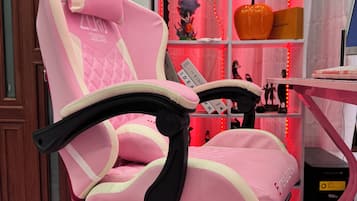 Una silla gamer rosa con reposabrazos y respaldo alto, ubicada frente a un escritorio con un monitor de computadora.