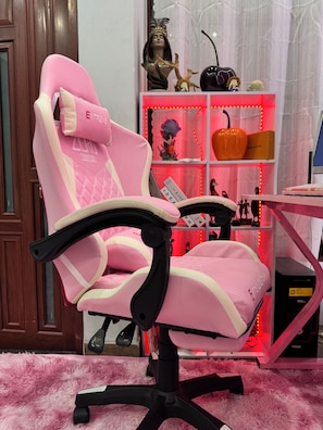A pink gaming chair with a high backrest and armrests, positioned in front of a desk with a computer monitor.