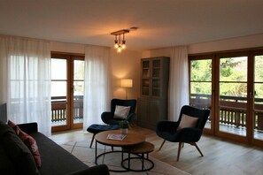 A room with a sofa, two armchairs, a table, a lamp, and a cabinet. There are large windows with curtains and a balcony visible through the windows. - Alpenflair Holiday Apartment 232 (Oberstdorf)