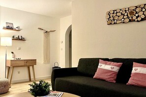 A living room with a dark sofa, a wooden desk, a lamp, and a wall-mounted decor piece. - Alpenflair Holiday Apartment 232 (Oberstdorf)