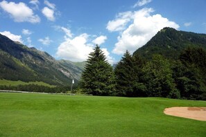 A golf course with a flag, trees, and mountains in the background. - Alpenflair Holiday Apartment 216 (Oberstdorf)