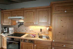 A kitchen with wooden cabinets, a stove, a sink, and a coffee maker. - Alpenflair Holiday Apartment 216 (Oberstdorf)