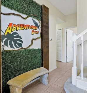 A hallway with a wall-mounted sign reading 'ADVENTURES Villa' and a stone bench. - Spacious 4-bedroom townhome in beautiful Kissimmee (Kissimmee)