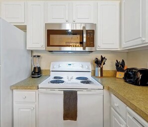 A kitchen with white cabinets, a microwave, a stove, a toaster, and a blender. - Spacious 4-bedroom townhome in beautiful Kissimmee (Kissimmee)