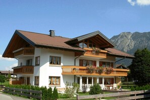 A two-story building with a balcony on the upper floor, surrounded by greenery and mountains in the background. - Alpenflair holiday apartment 241 (Oberstdorf)