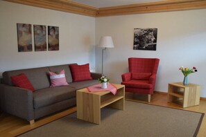 A living room with a sofa, a chair, a small table with a vase of flowers, and a lamp. - Alpenflair holiday apartment 241 (Oberstdorf)