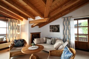 A cozy living room with a wooden ceiling, a sofa with patterned cushions, a round wooden table, and a bookshelf. - Alpenflair holiday apartment 230 (Oberstdorf)