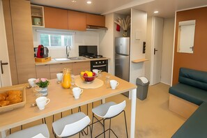A compact kitchen with a dining area, a refrigerator, and a seating area with a sofa. - Mobile Home '6 Pers Domaine La Yole' with Shared Pool, Private Terrace and Air Conditioning (Vendres)