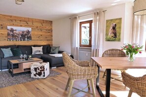 Ein gemütliches Wohnzimmer mit einer Couch, einem Couchtisch und Korbstühlen. Es steht ein Esstisch mit einer Blumenvase da.
