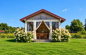 Eine Holzhütte mit rotem Dach, einem Essbereich mit Tisch und Stühlen sowie einem Garten mit weißen Blumen.