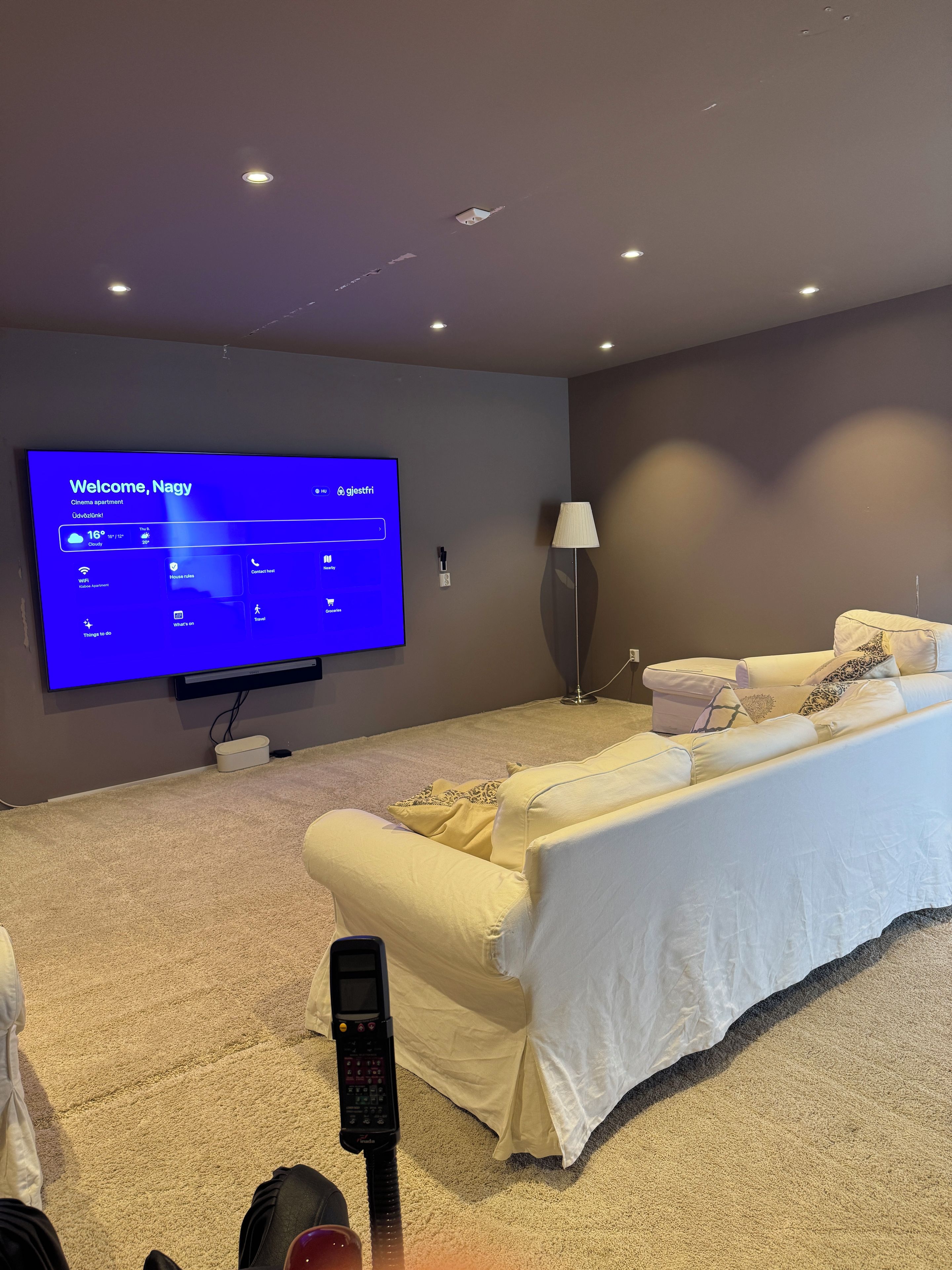 Un appartement moderne aménagé comme une salle de cinéma, avec un grand téléviseur à écran plat affichant un écran d’accueil, un fauteuil massant, un canapé et une lampe.