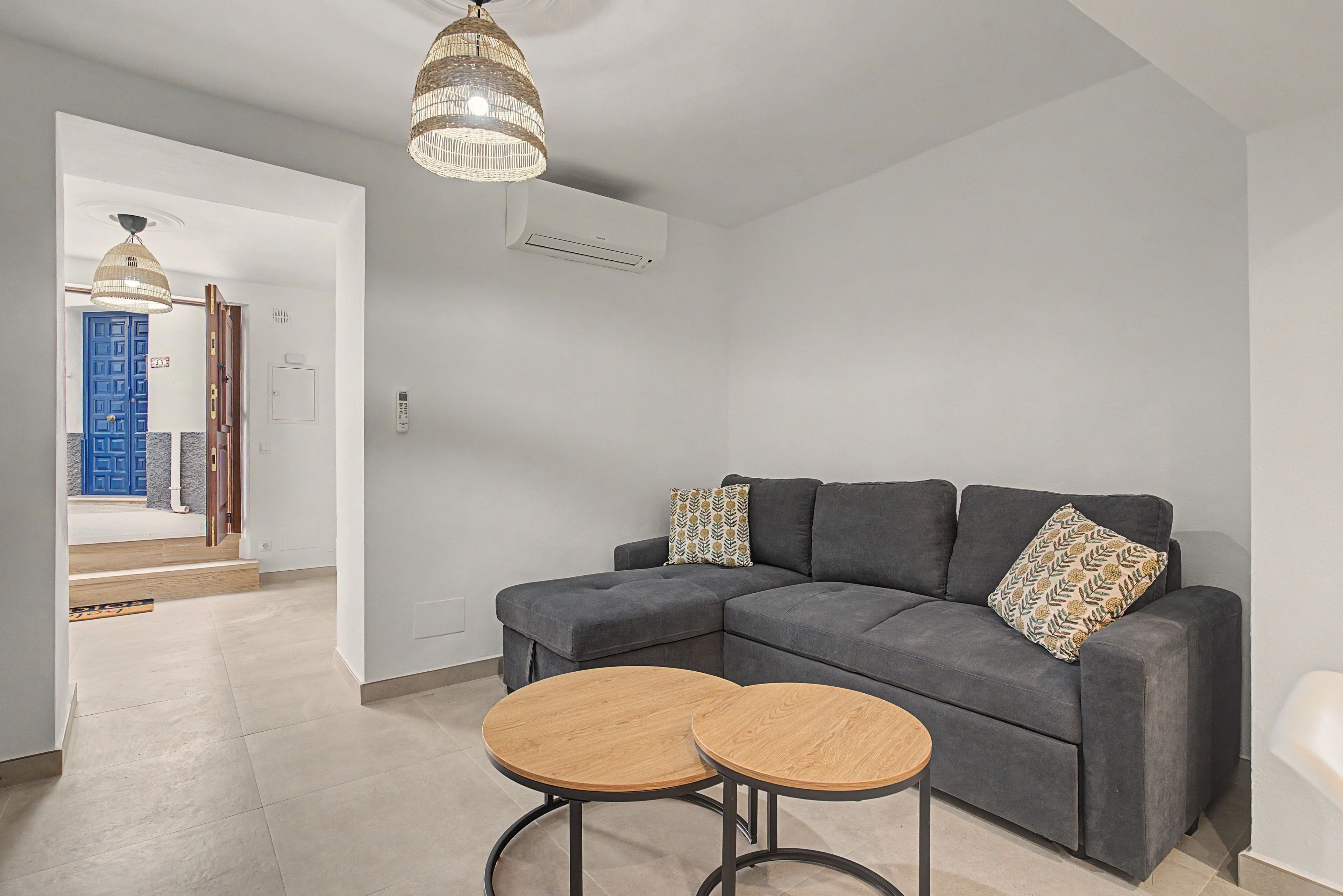 Una sala de estar moderna con un sofá seccional gris, dos mesas redondas de madera y una lámpara colgante.