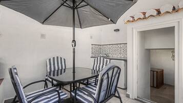 A dining area with a round table, four striped chairs, a large umbrella, and a patterned backsplash.