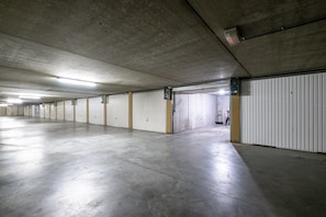Eine lange, leere Tiefgarage mit Betonböden und -wänden, mit mehreren geschlossenen Garagentoren.