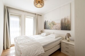 A bedroom with a large bed, two bedside tables, a wall-mounted lamp, and a painting. - Apartment in Zeedijk With Stunning Sea Views (Blankenberge)