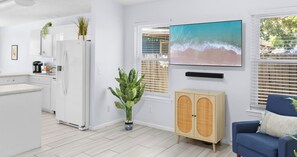 A modern living room with a blue sofa, a wooden cabinet, and a large window with blinds. - Pinetree Palace - 4BR Cozy Home (Panama City Beach)