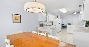 A modern kitchen with white cabinetry, a wooden dining table, and a hanging light fixture. - Pinetree Palace - 4BR Cozy Home (Panama City Beach)