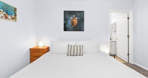 A bedroom with a bed, a nightstand, a wall-mounted picture, and a door. - Pinetree Palace - 4BR Cozy Home (Panama City Beach)