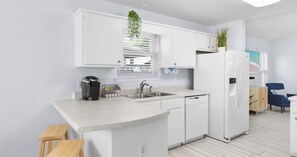 A modern kitchen with white cabinetry, a built-in dishwasher, and a coffee maker. - Pinetree Palace - 4BR Cozy Home (Panama City Beach)
