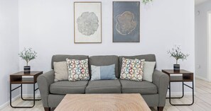 A living room with a grey sofa, patterned cushions, two side tables with potted plants, and two framed artworks on the wall. - Pinetree Palace - 4BR Cozy Home (Panama City Beach)