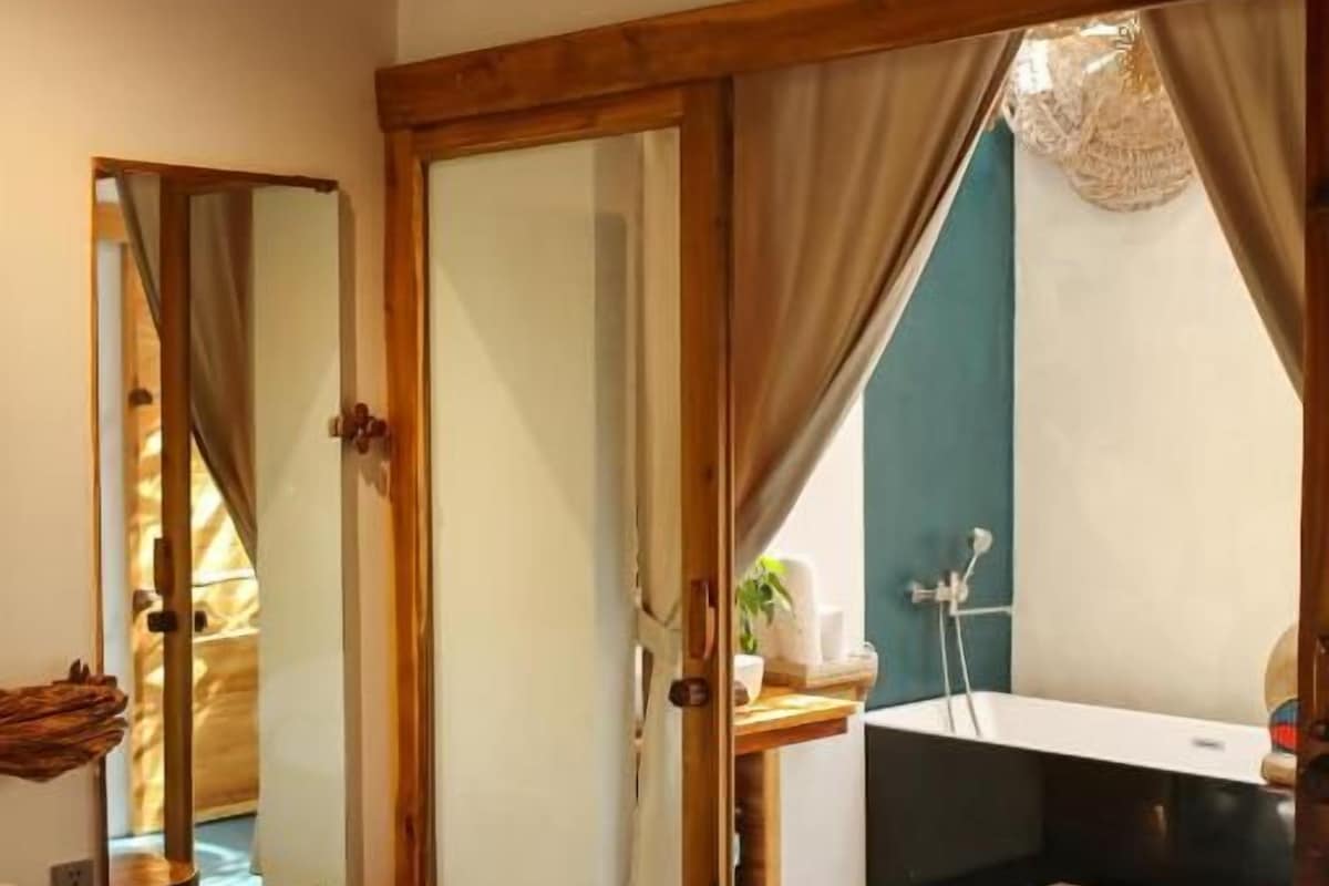Un dormitorio con cama, un baño con bañera y un ventanal amplio.