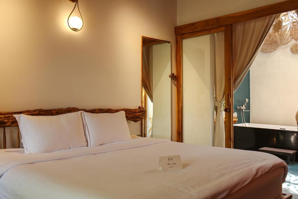 A hotel room with a bed, a bedside table, a mirror, and a window with curtains.