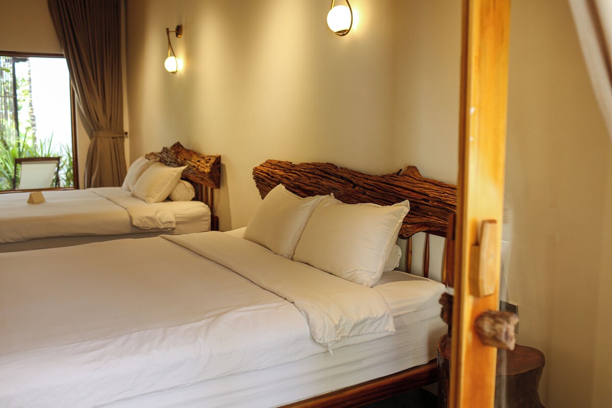 Une chambre d’hôtel avec deux lits, chacun doté de draps et d’oreillers blancs, d’une tête de lit en bois et d’une table de chevet avec une lampe.