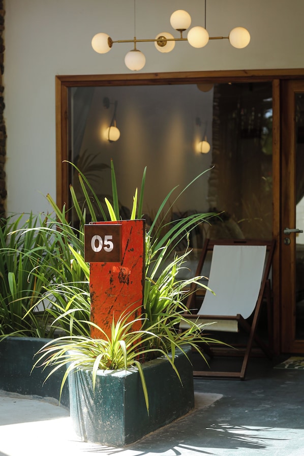 Entrada de un edificio con puerta de vidrio, un cartel con números y plantas en macetas.