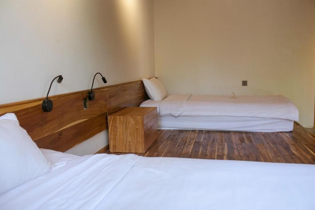 Ein Zimmer mit zwei Betten, einem Holzkopfstück, einem Nachttisch und Wandlampen.