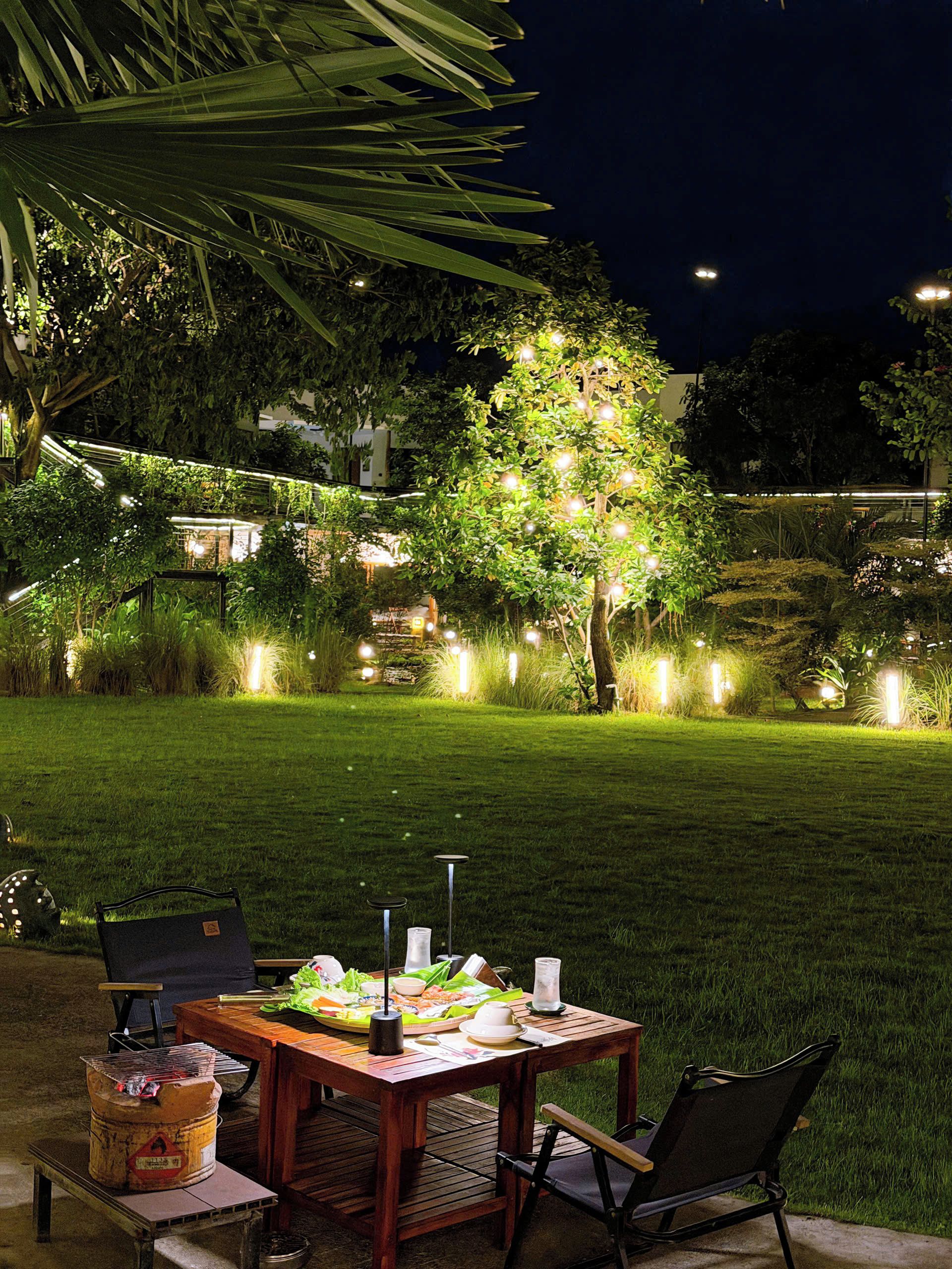 Uma área de refeições ao ar livre com uma mesa posta para dois, rodeada por vegetação exuberante e iluminada por luzes de Natal.