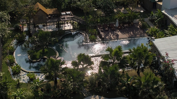 Vue aérienne d’un complexe hôtelier doté d’une grande piscine entourée de palmiers et d’une terrasse en bois.