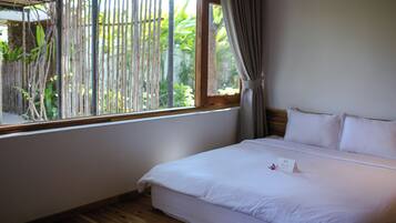 Quarto de hotel com uma cama, janela com vista para área verde e piso de madeira.