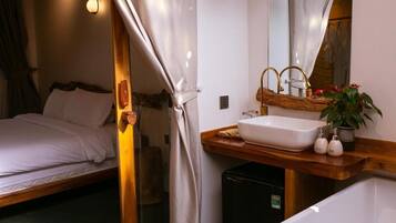 A hotel room with a bed, a wooden bedside table, a sink, and a mirror.