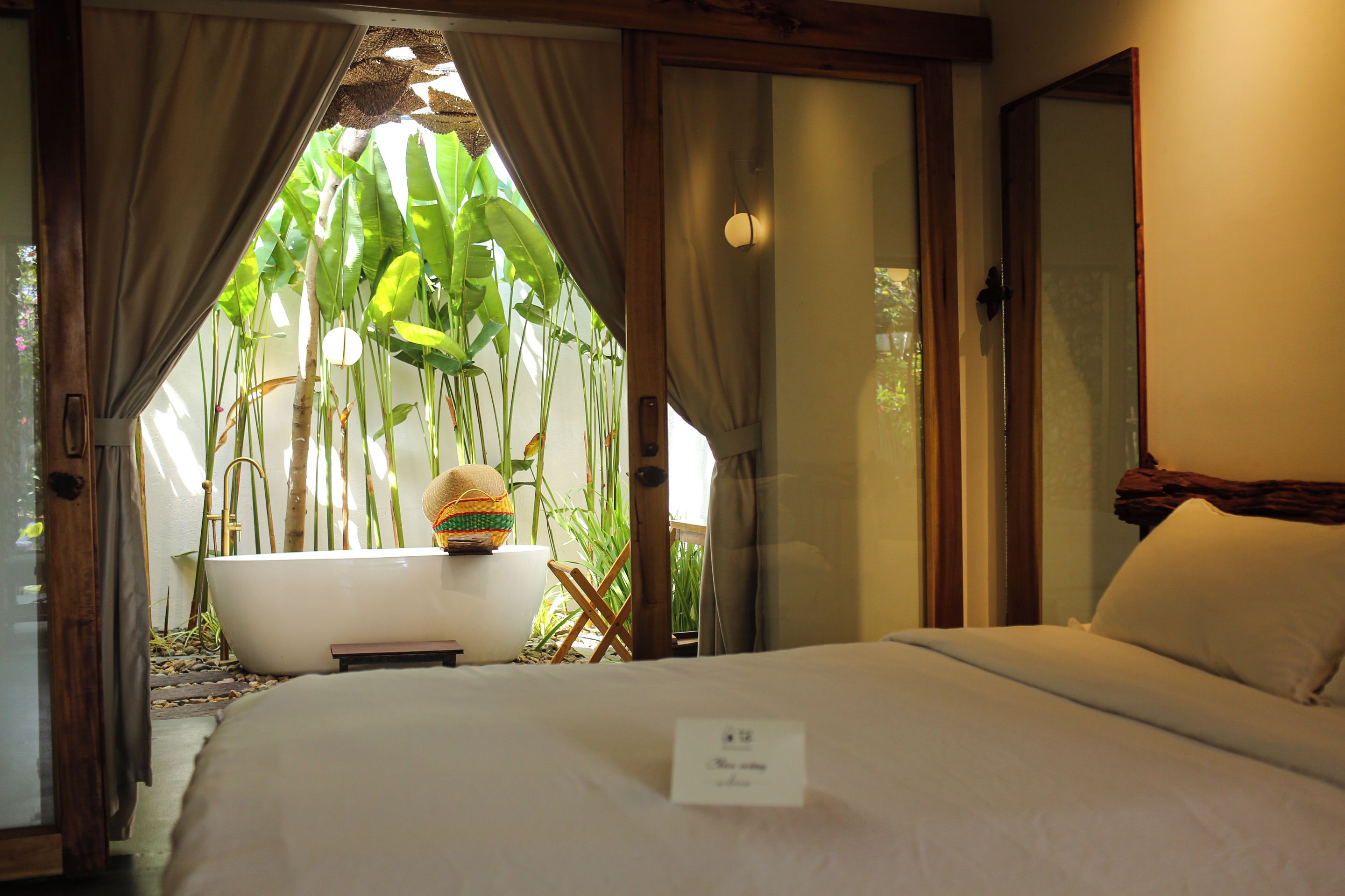 A hotel room with a bed, a bathtub, and a view of a tropical garden.