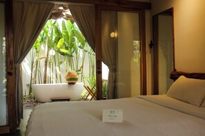 A hotel room with a bed, a bathtub, and a view of a tropical garden.