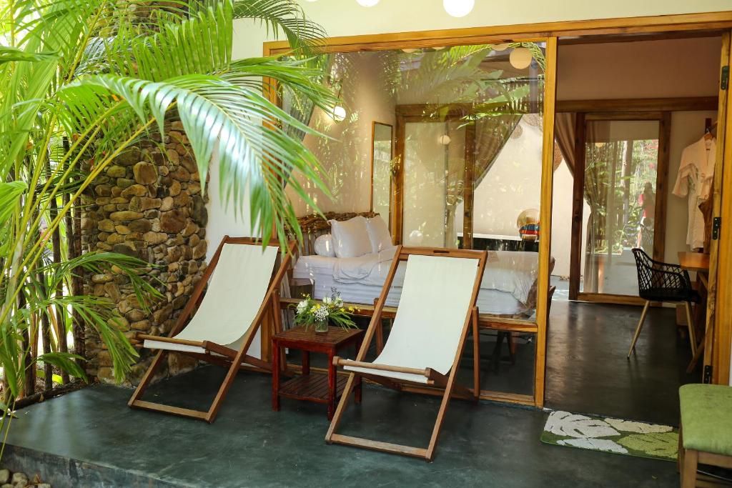 Una habitación con dos sillones, una pared de piedra y vista a un dormitorio a través de un vidrio.