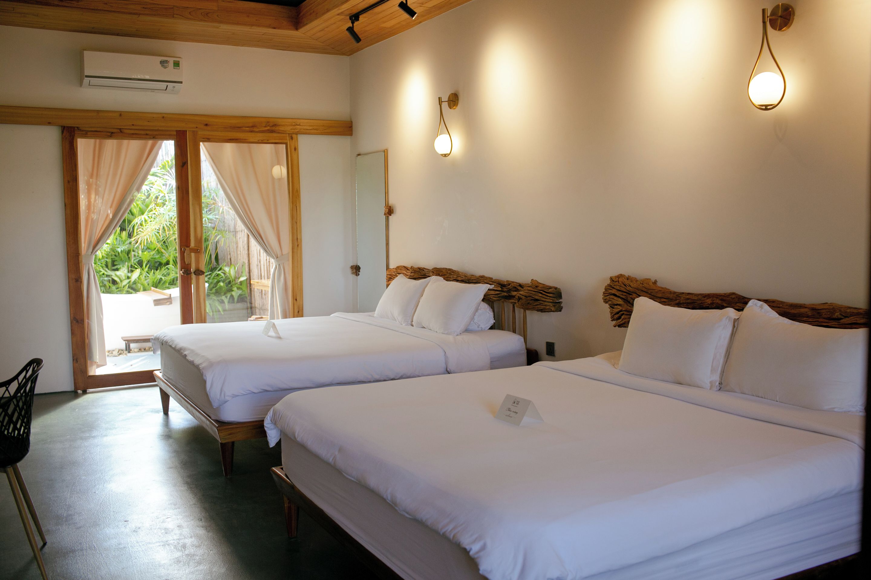 Une chambre d’hôtel avec deux lits, un plafond en bois, un grand miroir et une vue sur la verdure.