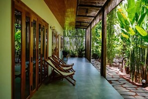 Un corredor cubierto con piso de madera, una zona de estar con sillones de madera y vistas a exuberante follaje.