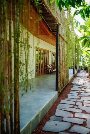 A pathway leading to a building with a wooden staircase and a covered area with chairs.