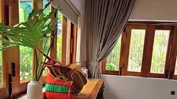 A dining area with a wooden table, chairs, a potted plant, and a window with curtains.